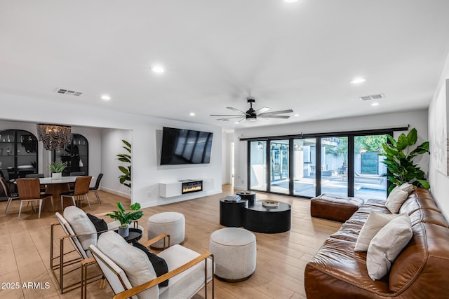 living area with visible vents, light wood-style floors, and ceiling fan with notable chandelier