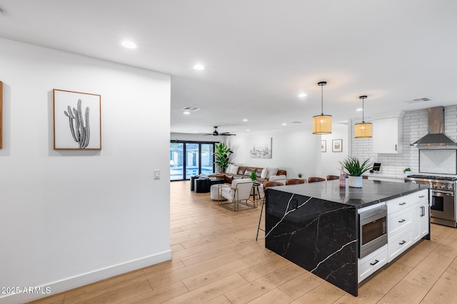 kitchen featuring wall chimney range hood, visible vents, appliances with stainless steel finishes, tasteful backsplash, and white cabinets
