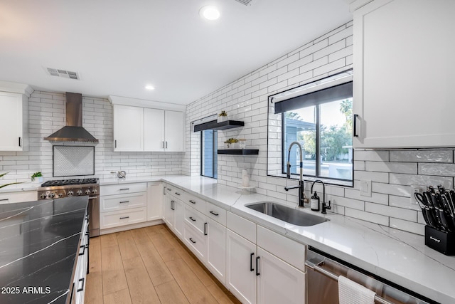 kitchen with wall chimney range hood, decorative backsplash, visible vents, a sink, and stainless steel appliances