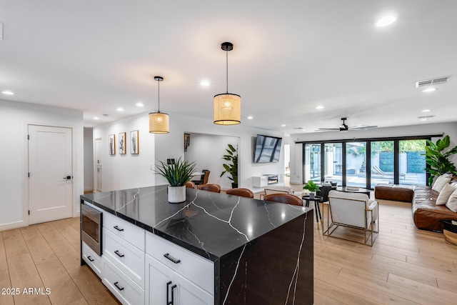 kitchen featuring recessed lighting, stainless steel microwave, open floor plan, and light wood finished floors