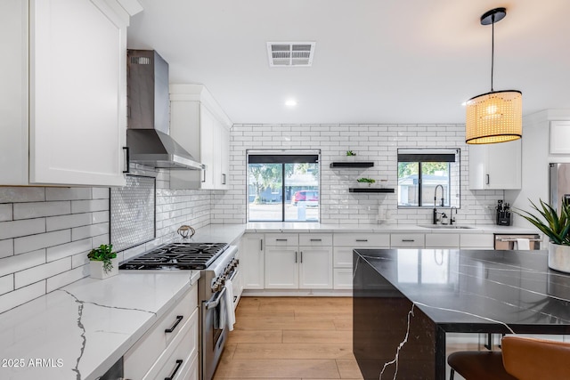 kitchen featuring visible vents, stainless steel stove, light wood-style floors, wall chimney range hood, and a sink