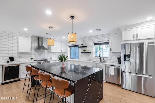 kitchen with beverage cooler, wall chimney range hood, a sink, appliances with stainless steel finishes, and backsplash