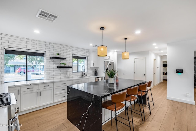 kitchen featuring visible vents, a kitchen breakfast bar, white cabinets, a sink, and appliances with stainless steel finishes