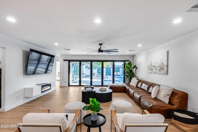 living area with ceiling fan, visible vents, light wood-type flooring, a glass covered fireplace, and recessed lighting
