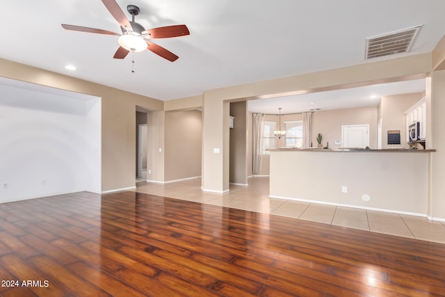 unfurnished living room featuring ceiling fan with notable chandelier and light wood-type flooring