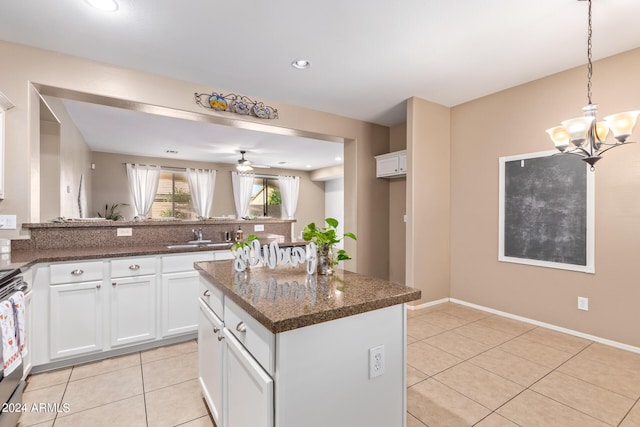 kitchen with dark stone countertops, white cabinetry, light tile patterned flooring, ceiling fan with notable chandelier, and a center island