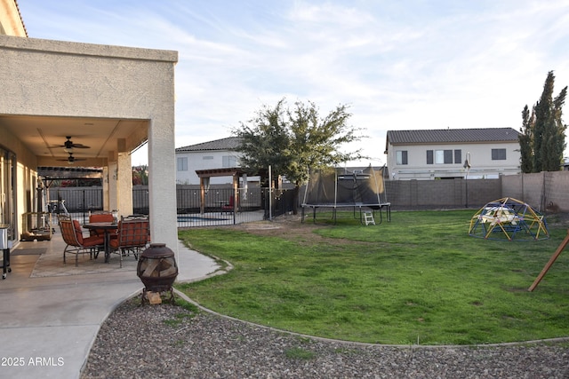 view of yard with a trampoline, a fire pit, ceiling fan, and a patio area