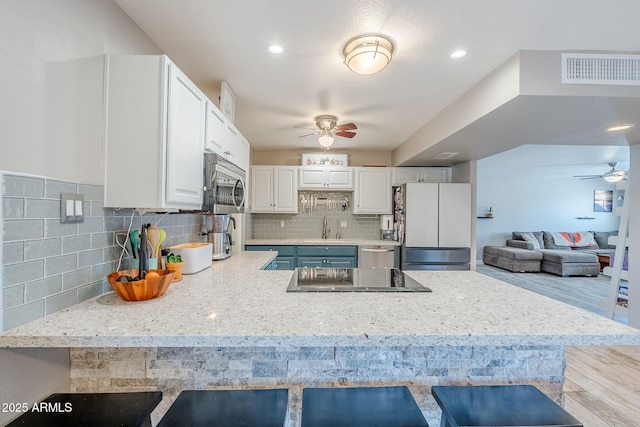 kitchen featuring visible vents, a breakfast bar area, appliances with stainless steel finishes, a peninsula, and a sink