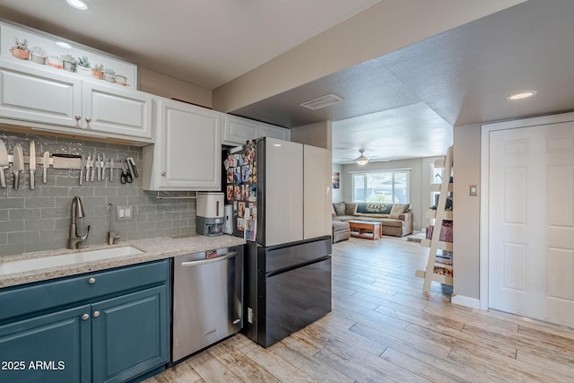 kitchen featuring light wood finished floors, freestanding refrigerator, a sink, dishwasher, and blue cabinets