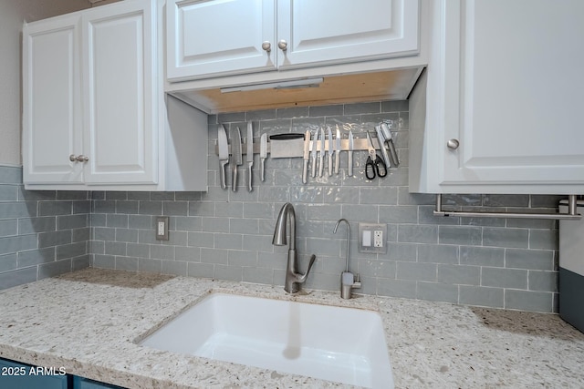 kitchen featuring decorative backsplash, white cabinets, light stone countertops, and a sink