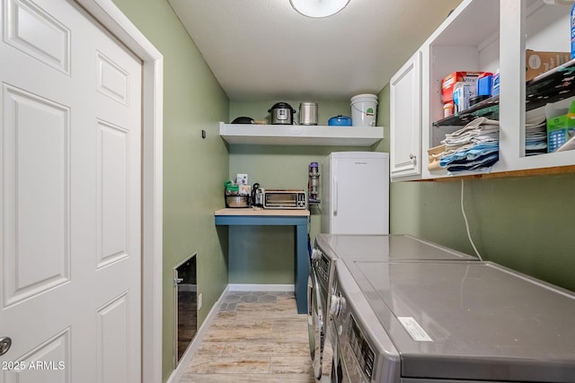 clothes washing area featuring light wood finished floors, baseboards, a toaster, washing machine and dryer, and cabinet space