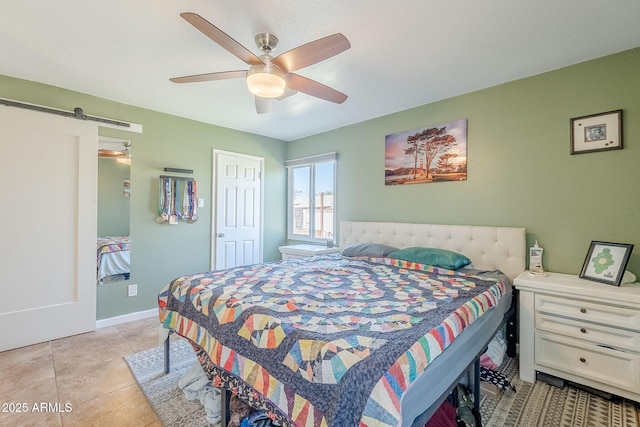 bedroom with a barn door, light tile patterned flooring, a ceiling fan, and baseboards