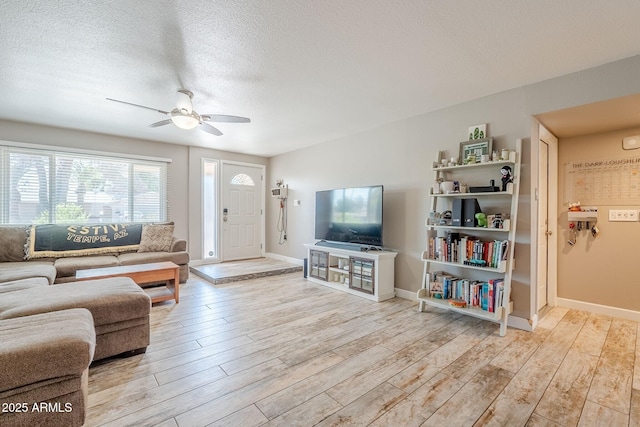 living room featuring baseboards, light wood-style flooring, a textured ceiling, and ceiling fan