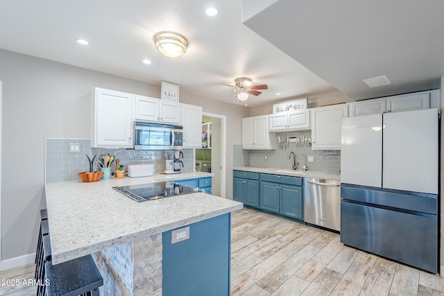 kitchen featuring visible vents, a peninsula, a sink, light countertops, and appliances with stainless steel finishes