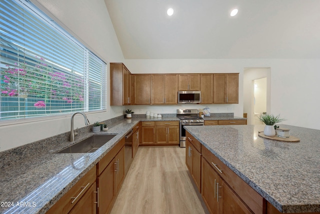 kitchen with light wood-type flooring, vaulted ceiling, sink, a center island, and appliances with stainless steel finishes