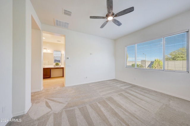 unfurnished bedroom featuring light colored carpet, ensuite bathroom, and ceiling fan