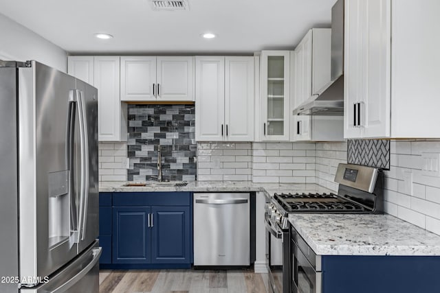 kitchen featuring white cabinetry, wall chimney range hood, stainless steel appliances, and blue cabinets