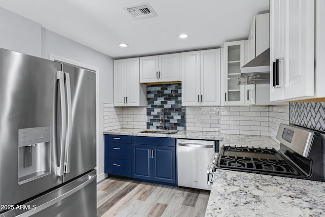 kitchen with sink, wall chimney range hood, white cabinetry, stainless steel appliances, and blue cabinets