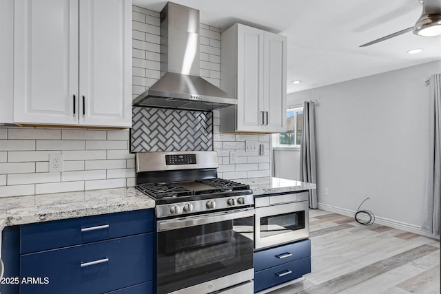 kitchen featuring wall chimney range hood, appliances with stainless steel finishes, light stone counters, white cabinets, and decorative backsplash