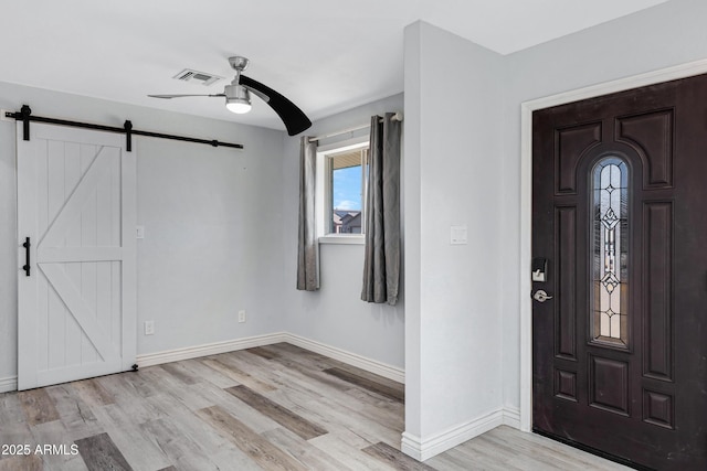 entryway with a barn door, ceiling fan, and light hardwood / wood-style flooring