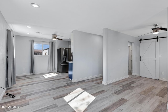 interior space with ceiling fan, a barn door, and light hardwood / wood-style floors