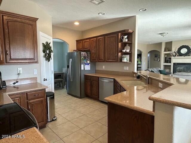 kitchen with sink, built in shelves, light tile patterned flooring, kitchen peninsula, and stainless steel appliances