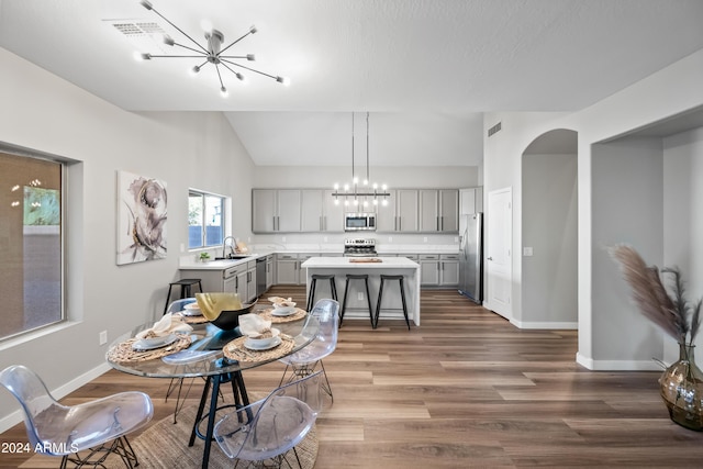 dining space with vaulted ceiling, hardwood / wood-style flooring, an inviting chandelier, and sink