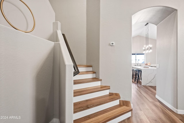 stairway with a chandelier, hardwood / wood-style flooring, vaulted ceiling, and sink