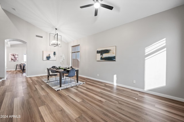 dining space with ceiling fan with notable chandelier, hardwood / wood-style flooring, and high vaulted ceiling