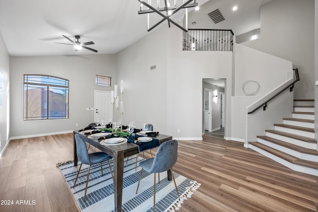 dining space with ceiling fan with notable chandelier, hardwood / wood-style flooring, and high vaulted ceiling