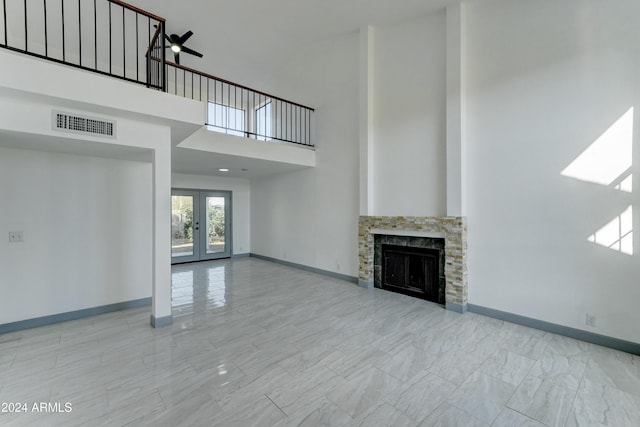 unfurnished living room with a stone fireplace, ceiling fan, french doors, and a towering ceiling