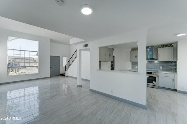 kitchen featuring tasteful backsplash, gray cabinetry, wall chimney exhaust hood, and appliances with stainless steel finishes