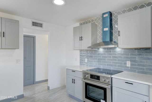 kitchen featuring gray cabinetry, backsplash, stainless steel range with electric cooktop, and wall chimney range hood