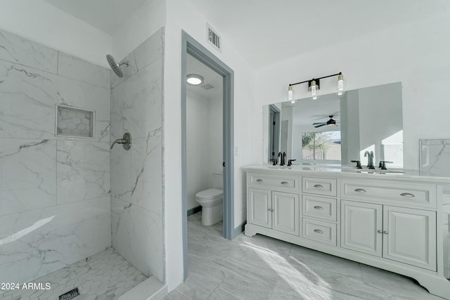 bathroom with a tile shower, vanity, toilet, and ceiling fan