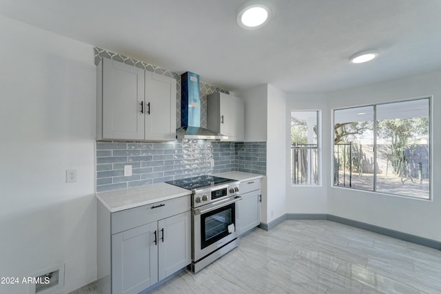 kitchen with gray cabinetry, high end stove, wall chimney range hood, and tasteful backsplash