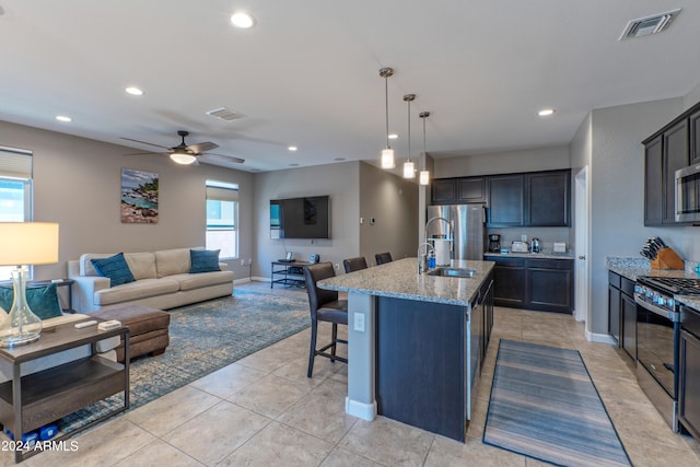 kitchen featuring ceiling fan, a healthy amount of sunlight, light stone countertops, an island with sink, and stainless steel appliances