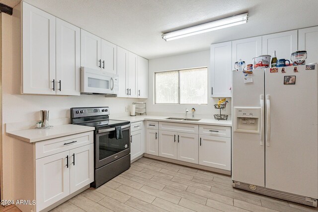 kitchen featuring sink, white cabinets, white appliances, a textured ceiling, and light hardwood / wood-style flooring