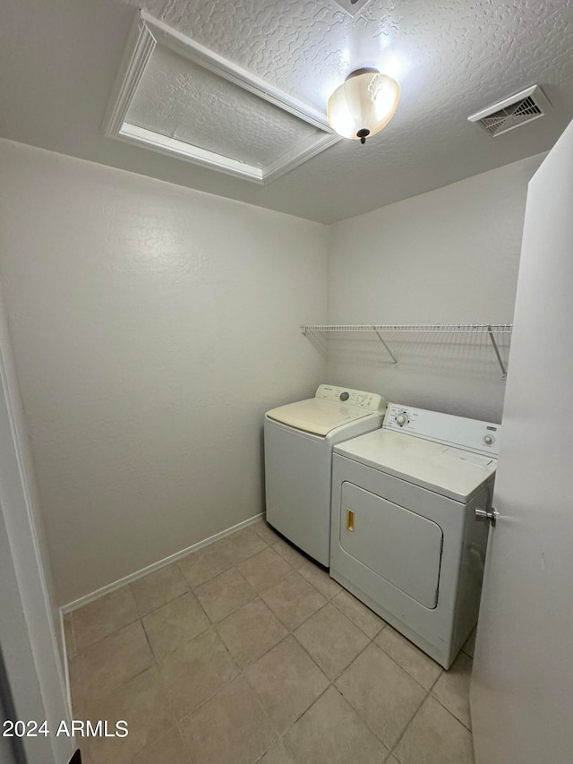 washroom featuring a textured ceiling, light tile patterned floors, and washing machine and clothes dryer