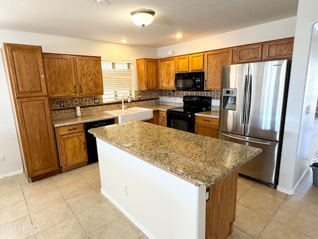 kitchen with sink, black appliances, a center island, light stone countertops, and decorative backsplash