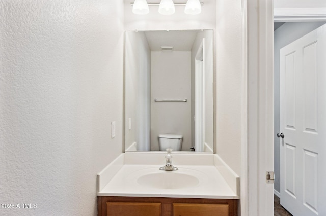 bathroom featuring a textured wall, vanity, and toilet