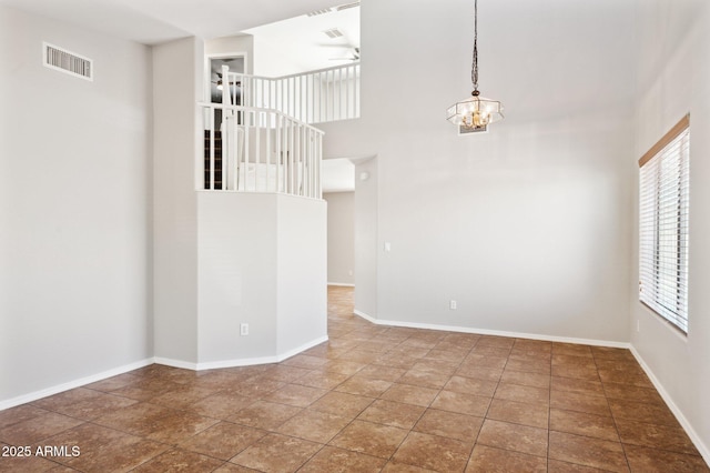 empty room featuring a chandelier, a ceiling fan, baseboards, and a towering ceiling