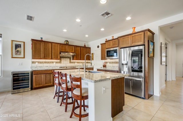 kitchen featuring stainless steel refrigerator, a kitchen island with sink, tasteful backsplash, built in microwave, and beverage cooler