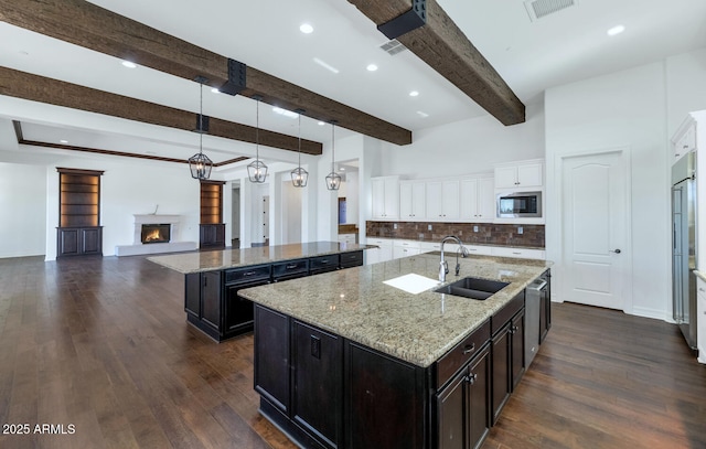 kitchen with a kitchen island with sink, sink, beam ceiling, built in appliances, and white cabinets