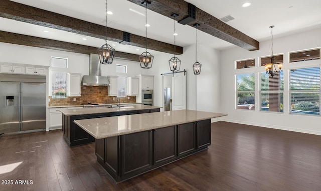 kitchen with light stone counters, stainless steel appliances, pendant lighting, beamed ceiling, and white cabinets