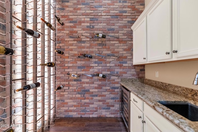 wine room featuring wine cooler, sink, brick wall, and dark wood-type flooring