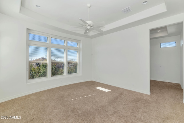 empty room featuring a tray ceiling, light carpet, and ceiling fan