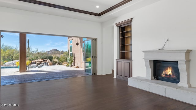 unfurnished living room with ornamental molding, a raised ceiling, a tile fireplace, built in features, and hardwood / wood-style floors