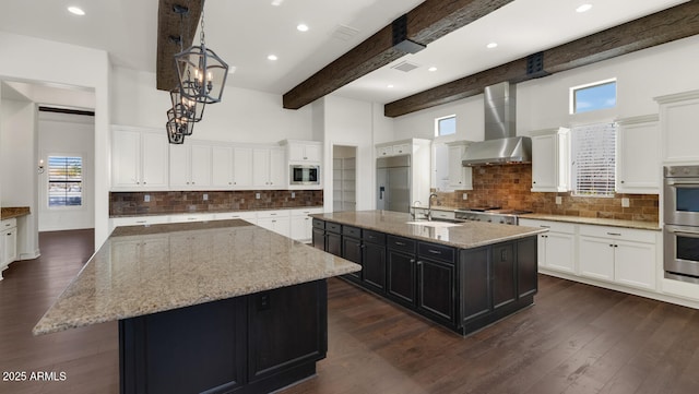 kitchen with white cabinetry, a large island, wall chimney range hood, beamed ceiling, and built in appliances