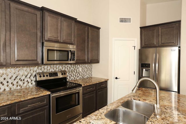 kitchen with dark brown cabinetry, light stone countertops, sink, stainless steel appliances, and backsplash