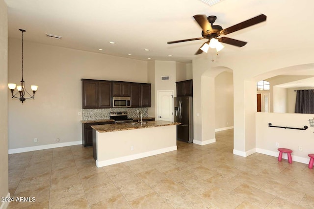 kitchen with hanging light fixtures, dark stone countertops, a kitchen island with sink, ceiling fan with notable chandelier, and appliances with stainless steel finishes